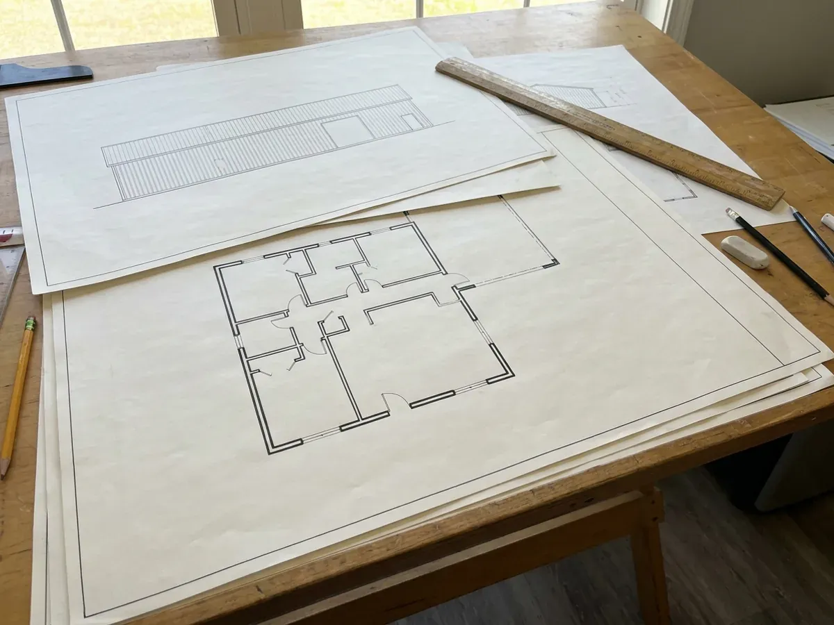Barndominium floor plan and elevation drawings laid out on a drafting table with a scale rule.