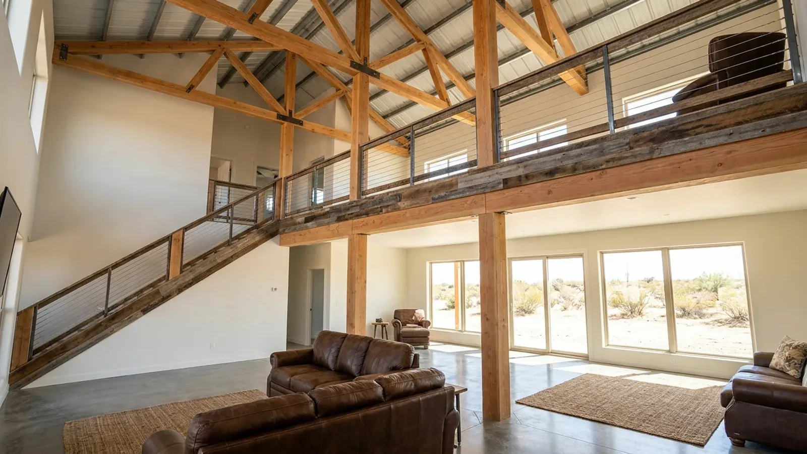 A barndominium great room with an open loft level and railing built over part of the room, reached by an open staircase.